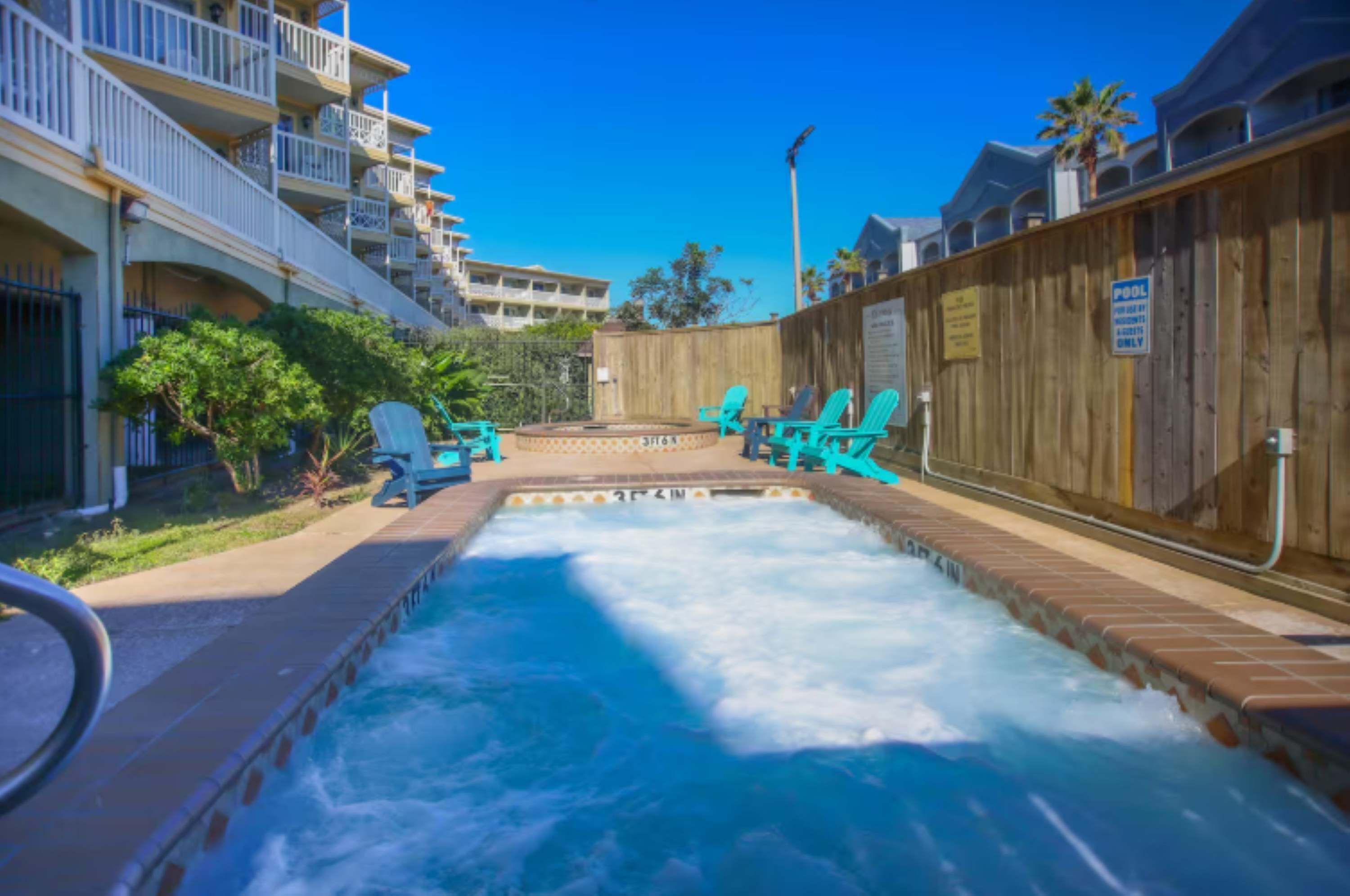 Un espace avec un jacuzzi, entouré d’une clôture en bois, une piscine et des chaises longues.