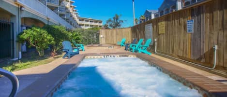 Un espace avec un jacuzzi, entouré d’une clôture en bois, une piscine et des chaises longues.