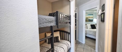 Uma cama de beliche com roupa de cama estampada e um corredor que dá para um quarto com uma cama e um quadro na parede.