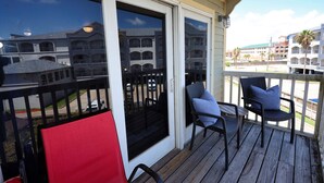 A wooden deck with outdoor seating and a view of a multi-story building. - Seawall Serenity - Amenities (Galveston)