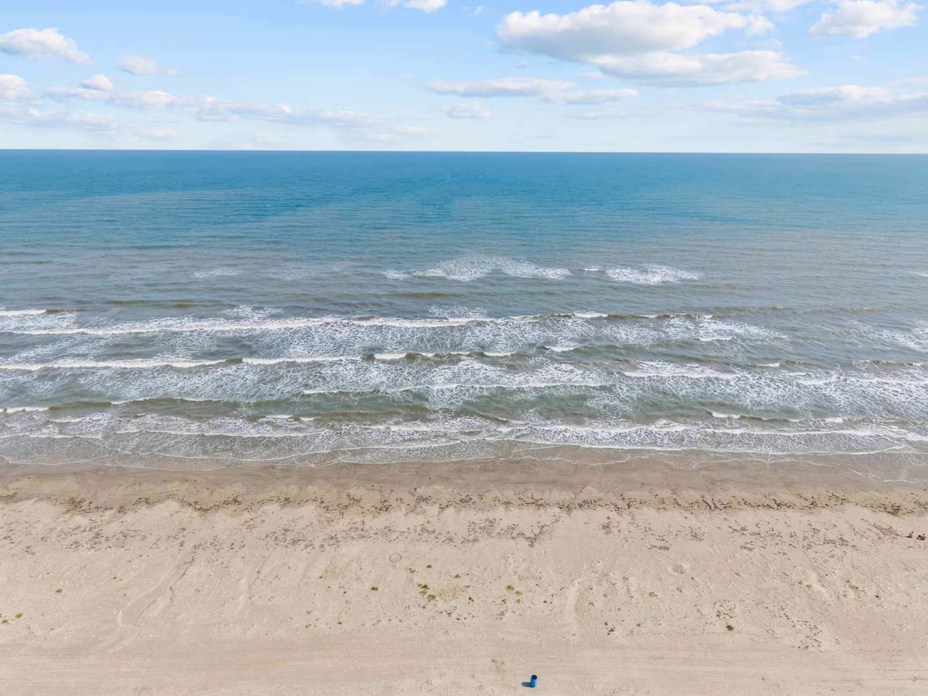 Una playa con olas acercándose a la orilla, cielos despejados y un horizonte lejano.