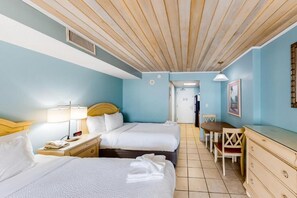 Habitación de hotel con dos camas, un escritorio, una silla, una cómoda y una puerta que da a otra habitación.