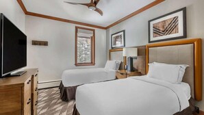 Quarto de hotel com duas camas, uma televisão, uma janela com vista para árvores e obras de arte emolduradas nas paredes.