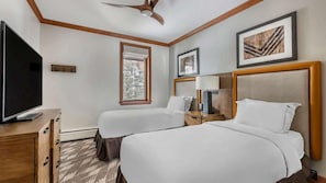 A hotel room with two beds, a television, a window with a view of trees, and framed artwork on the walls.