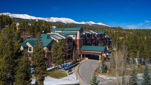 Uma hospedaria com vários edifícios, um teleférico e montanhas cobertas de neve ao fundo.