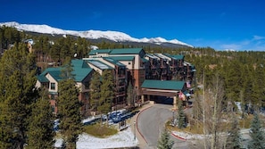 A lodge with multiple buildings, a ski lift, and snow-covered mountains in the background.