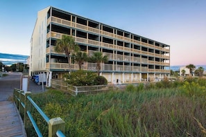 Un hotel de varios pisos con balcones, un estacionamiento y un paseo marítimo que conduce al edificio.