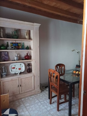 A dining area with a wooden table and chairs, a cabinet with various kitchenware, and a tiled floor.