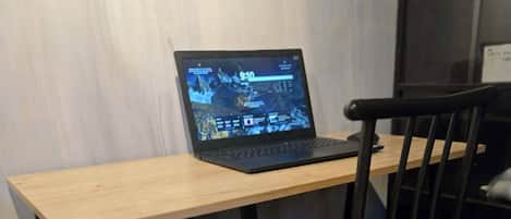 A small, compact workspace with a laptop on a wooden desk, a chair, and a small table.