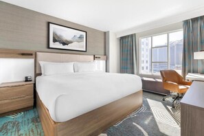 Habitación de hotel con una cama grande, un escritorio, una silla y una ventana con cortinas.