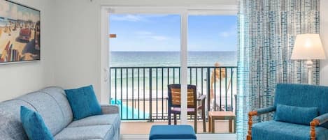 A room with a sofa, a chair, a table, and a view of the sea through a sliding door.