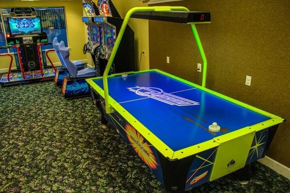 A pool table with a neon green frame, a digital score display, and arcade machines in the background. - Beachfront 2BR Retreat | Balcony + Full Kitchen (Cocoa Beach)