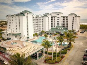 A multi-story hotel with a pool area, palm trees, and a view of the ocean. - Beachfront 2BR Retreat | Balcony + Full Kitchen (Cocoa Beach)