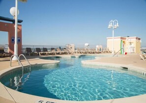 A pool area with lounge chairs, a pool ladder, and a no lifeguard sign. - Oceanfront 2BR | Balcony, Pools & Lazy River (North Myrtle Beach)