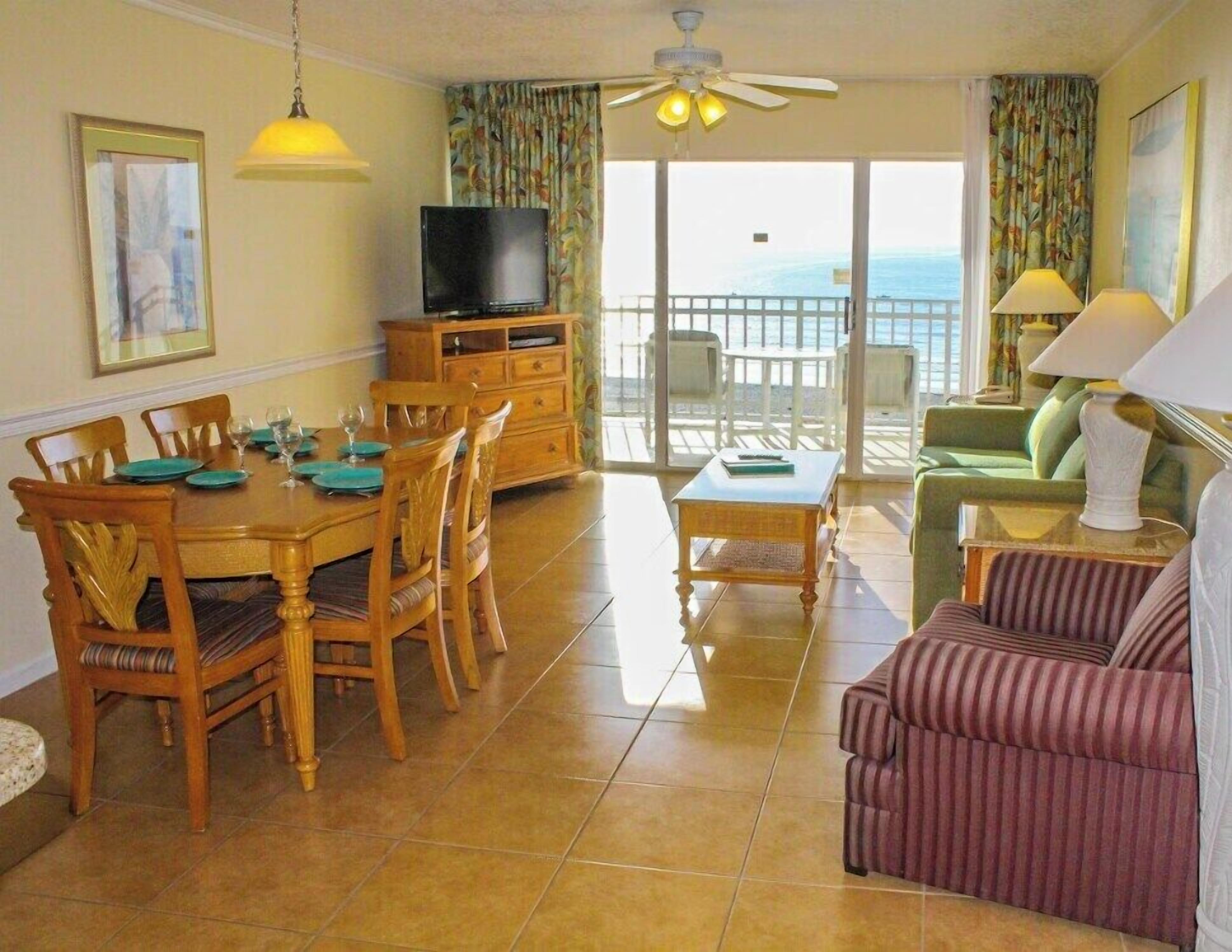 Un coin repas avec une table et des chaises en bois, un téléviseur posé sur un meuble, et un balcon avec vue.