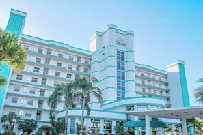 Un hotel de varios pisos con una fachada curva distintiva, balcones en cada planta y una torre central con un ventanal circular.