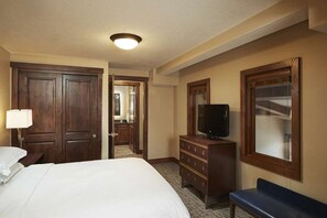 Quarto de hotel com uma cama grande, penteadeira, televisão e um banco.