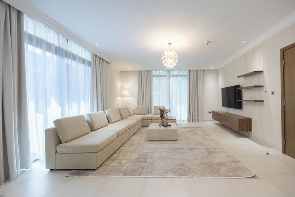 A modern living room with a sectional sofa, a coffee table, a TV, and a chandelier.