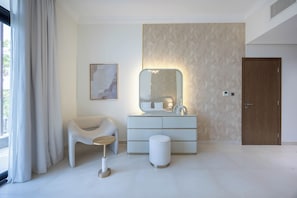 A modern bedroom with a large mirror, a bedside table, a chair, and a wooden door. - Bloomfields 5BR+ 2M Villa in West Yas (Abu Dhabi)
