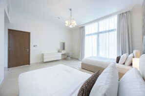 A modern bedroom with two beds, a dresser, a chandelier, and large windows with curtains. - Bloomfields 5BR+ 2M Villa in West Yas (Abu Dhabi)