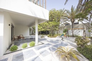 A modern outdoor patio area with a covered seating area, a children's play structure, and a variety of plants.