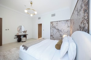 A modern bedroom with a large bed, a bedside table, a mirror, and a decorative wall panel.
