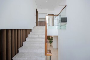 A modern staircase with a glass railing, leading to a second-floor area with a kitchen and a seating area.