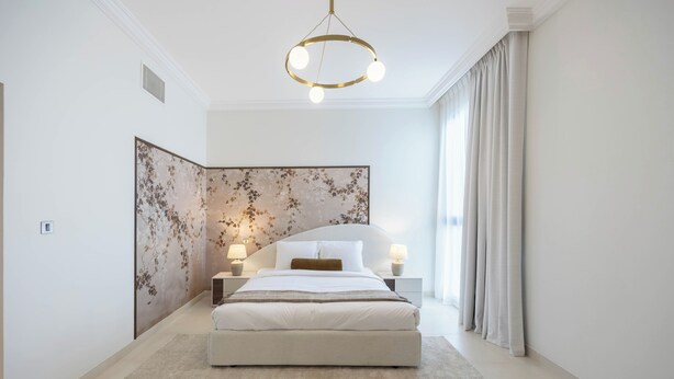 Quarto moderno com cama grande, duas luminárias de cabeceira, um painel decorativo na parede e um lustre.