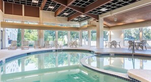 Piscina interna com vista clara para o exterior, rodeada por espreguiçadeiras e mesas.