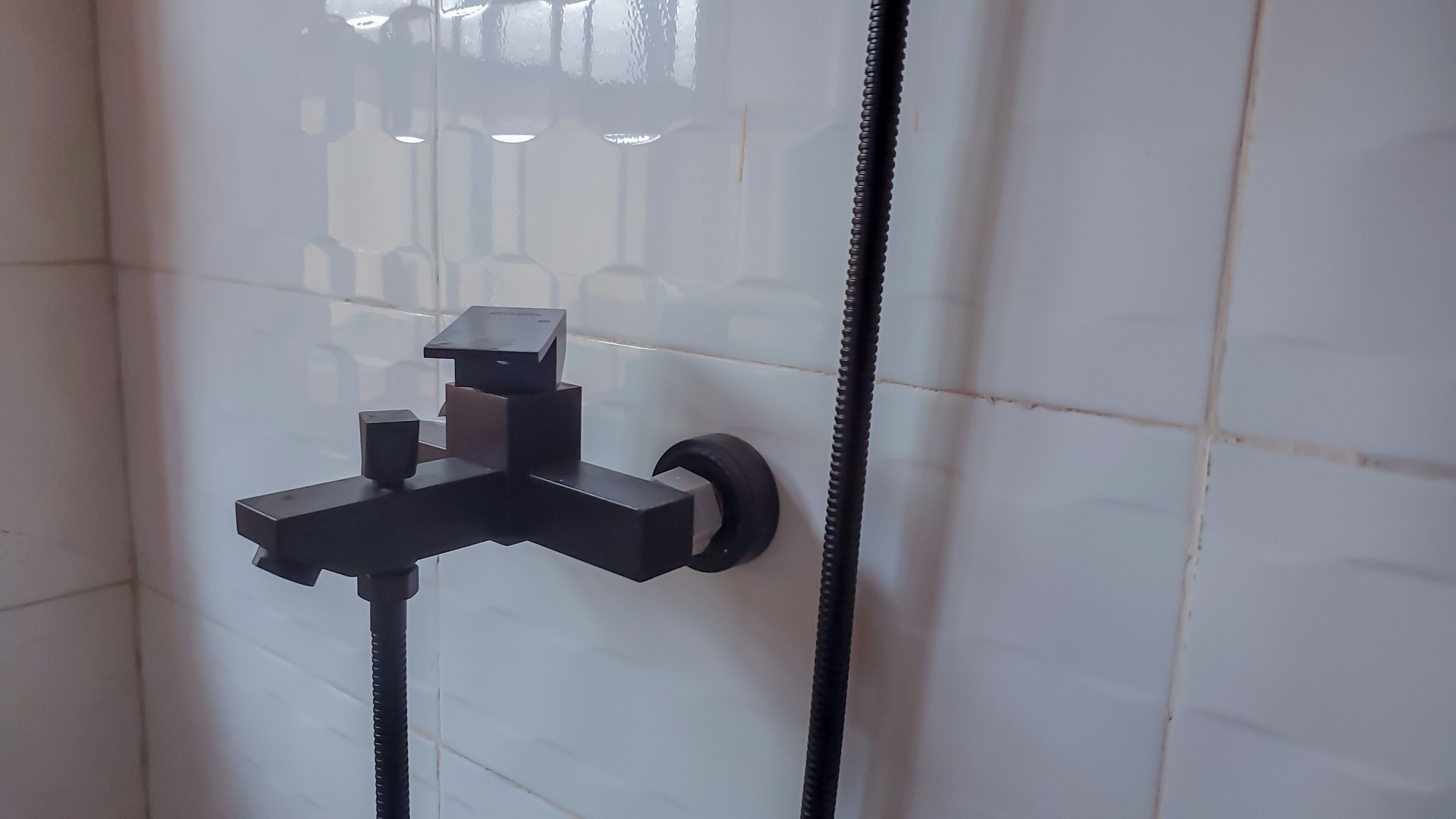Une salle de bain équipée d’un système de douche moderne, comprenant un pommeau de douche à main et un pommeau de douche fixe.