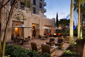 An outdoor patio area with seating and tables, a fire feature, and a Ferris wheel in the background. - Family suite close to Disney & I-Drive (Orlando)