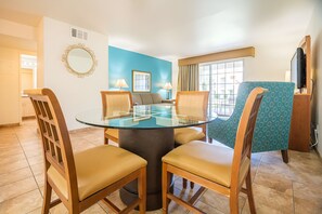 A dining area with a glass-top table surrounded by wooden chairs, a blue wall, and a window with curtains. - Relaxing 1BR Desert w/ Pool & Parking (Palm Desert)