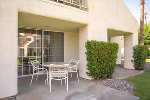 A patio with a table and chairs, a glass door, and a hedge. - Relaxing 1BR Desert w/ Pool & Parking (Palm Desert)