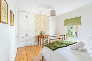 A bedroom with a bed, a wooden floor, a wardrobe, a desk, and a window with a view. - A comfortable two bedroom terrace house in NR2, sleeping four across two rooms, one with en suite shower-room. Free on street parking and log burner. (Norwich)