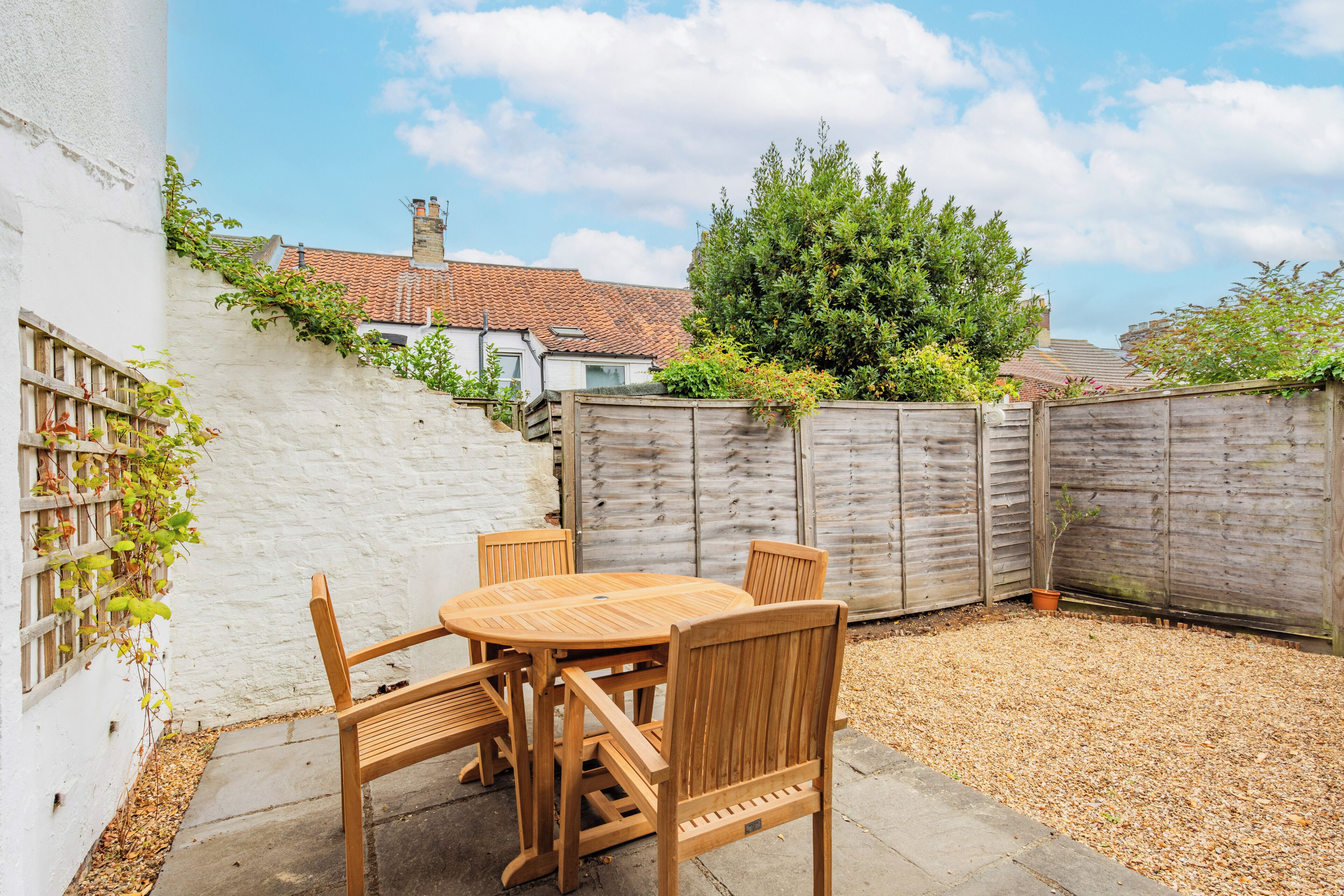A patio with a wooden table and chairs, surrounded by a white wall and a wooden fence.