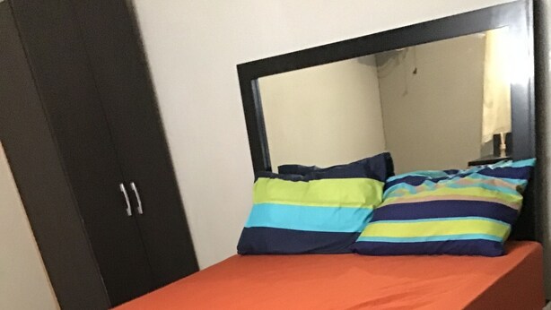 A bed with a red mattress and a dark blue blanket, a mirror above the bed, and a wardrobe to the left.