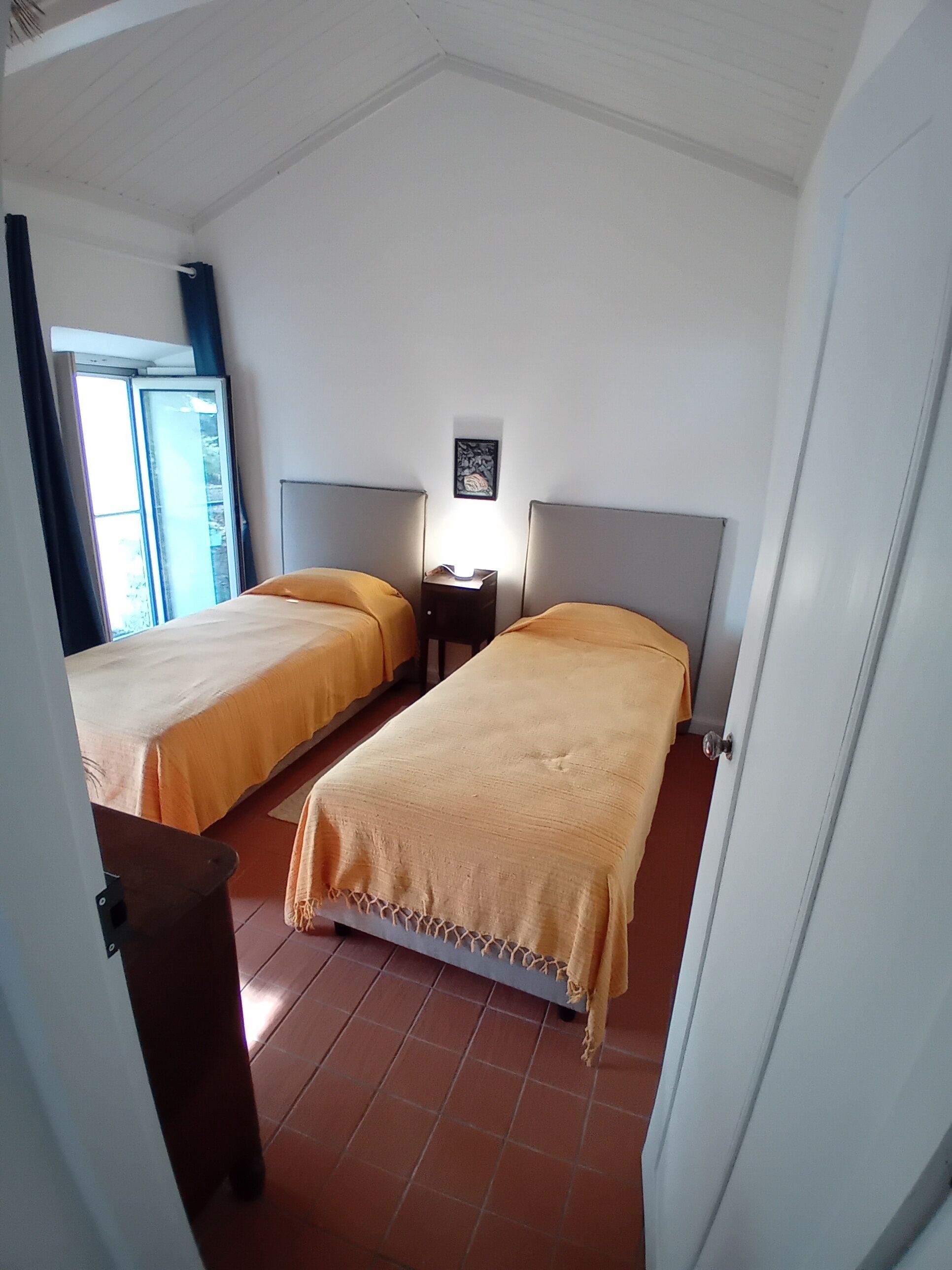 Ein Zimmer mit zwei Betten, einem Nachttisch, einer Wandlampe und einem Fenster mit Vorhängen.