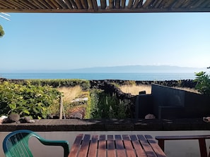 Taula i caires de fusta en un balcó amb vista a un paisatge costaner, amb una vista clara del mar i muntanyes llunyanes.
