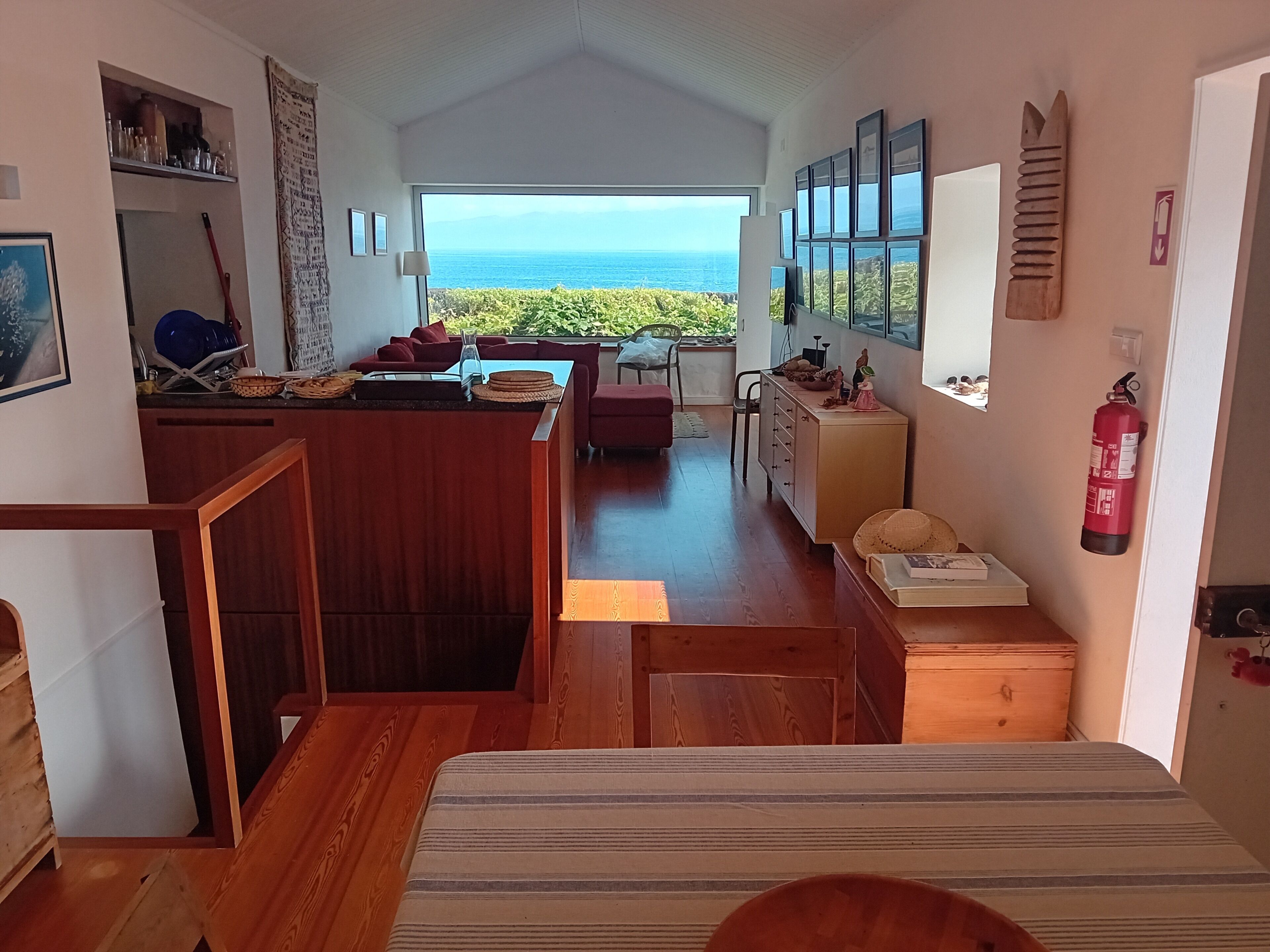A spacious room with a view of the ocean, a wooden dining area, and a kitchen with a fire extinguisher.