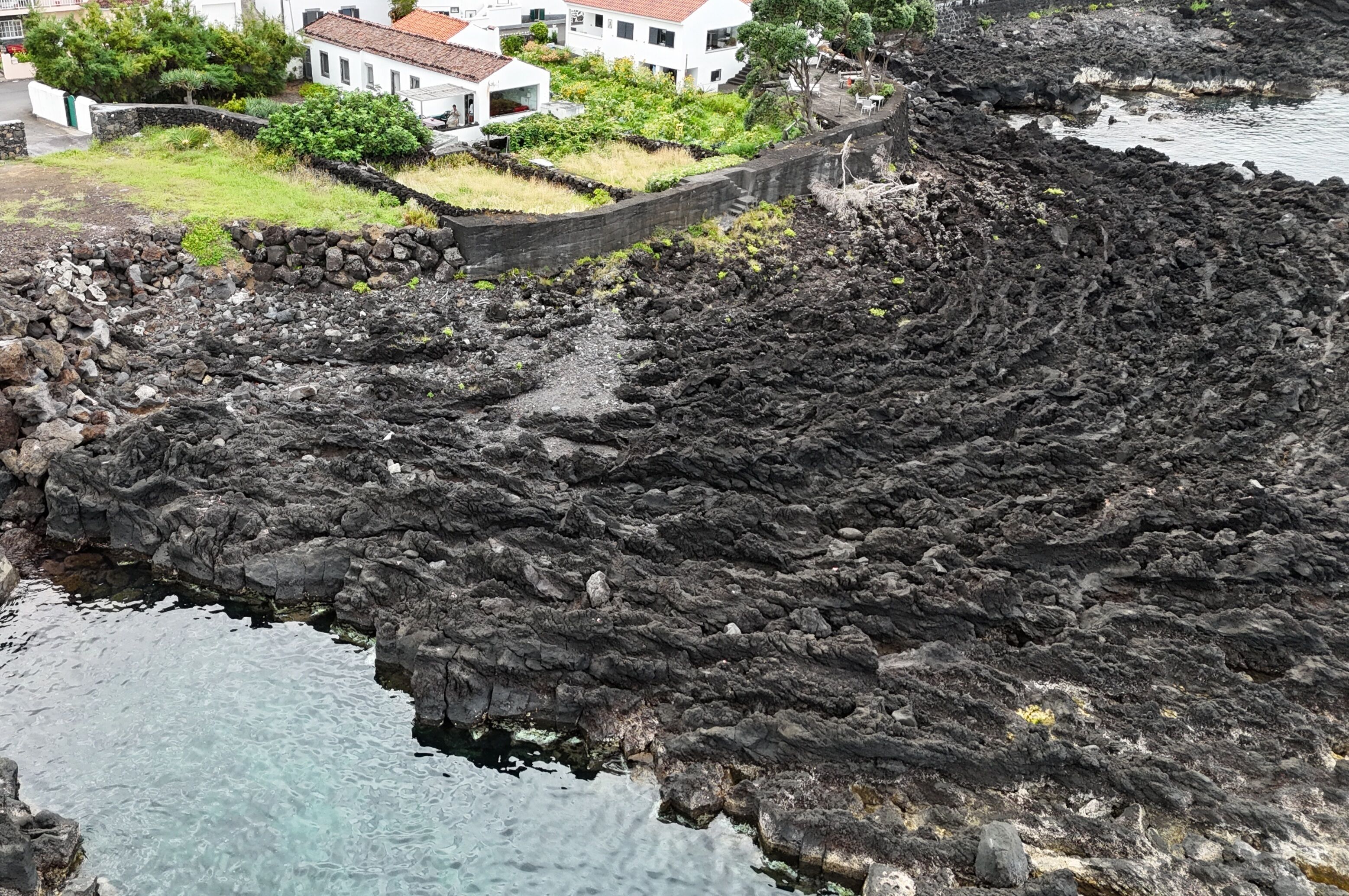 Uma área costeira com terreno rochoso e um edifício residencial com telhado de telhas vermelhas.