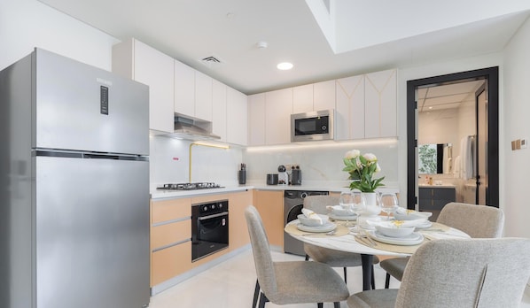 A modern kitchen with a stainless steel refrigerator, a microwave, and a dining area with a round table set for four. - Vogue | Skyz by Danube near Dubai Miracle Garden (Dubai)