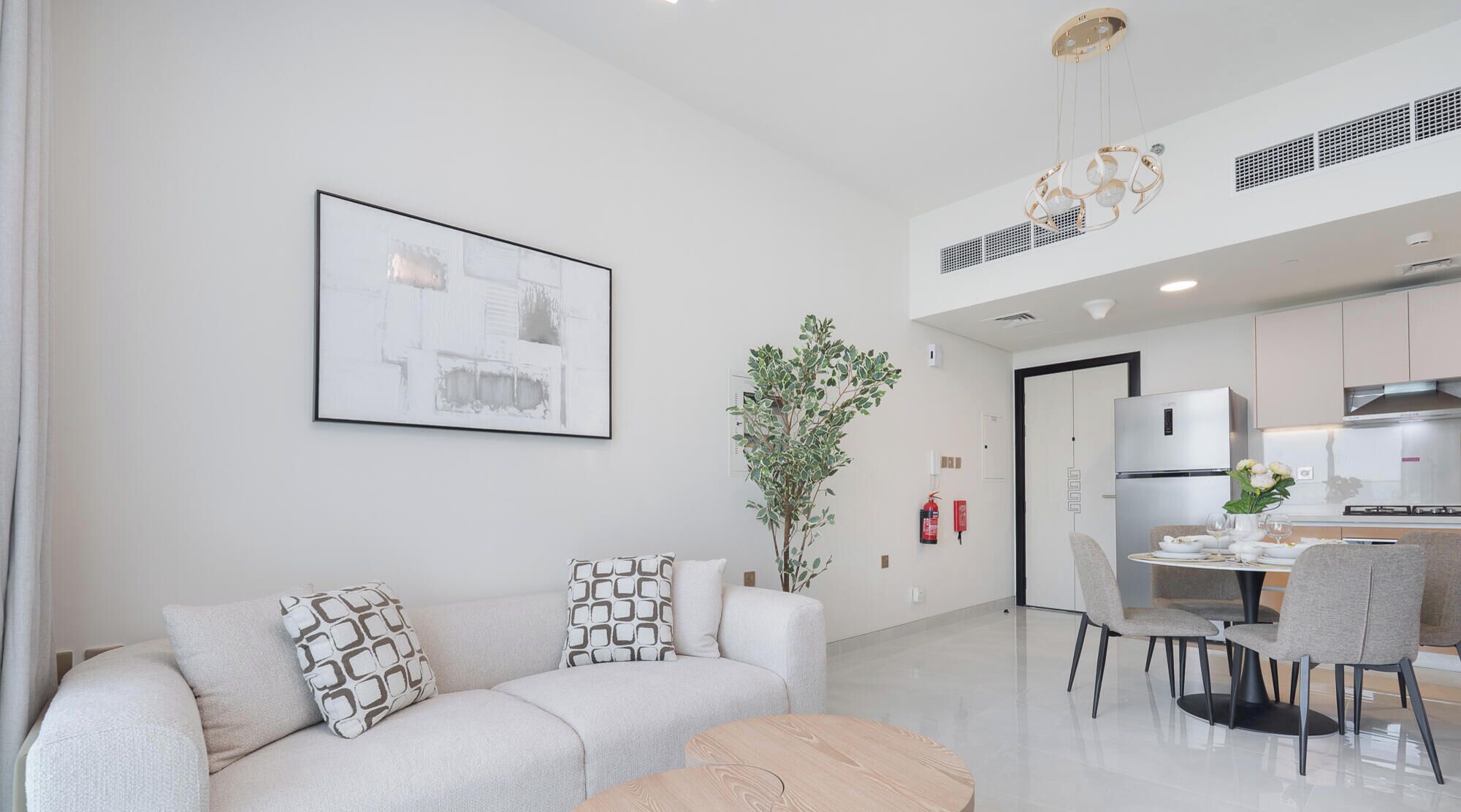Un salon moderne comprenant un canapé, un coin repas avec des chaises, une cuisine équipée et un luminaire au plafond.