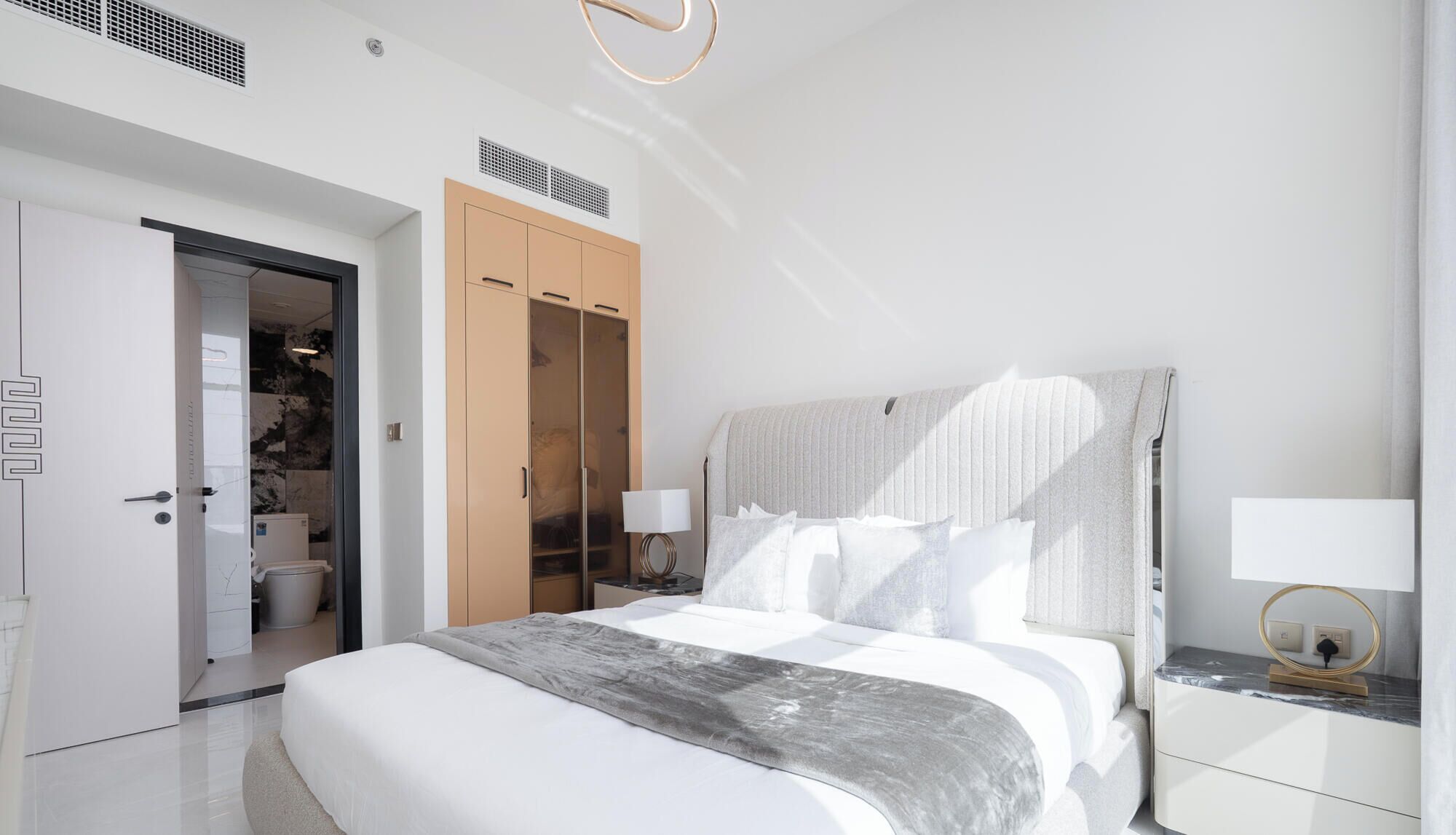 Ein modernes Schlafzimmer mit einem großen Bett, einem Kleiderschrank und einem durch eine offene Tür einsehbarer Badezimmer.