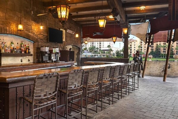 A bar area with a long counter, wicker chairs, and hanging lanterns. - Resort 2BR Suite | King Bed, Balcony & 2 Bathrooms (Lake Buena Vista)