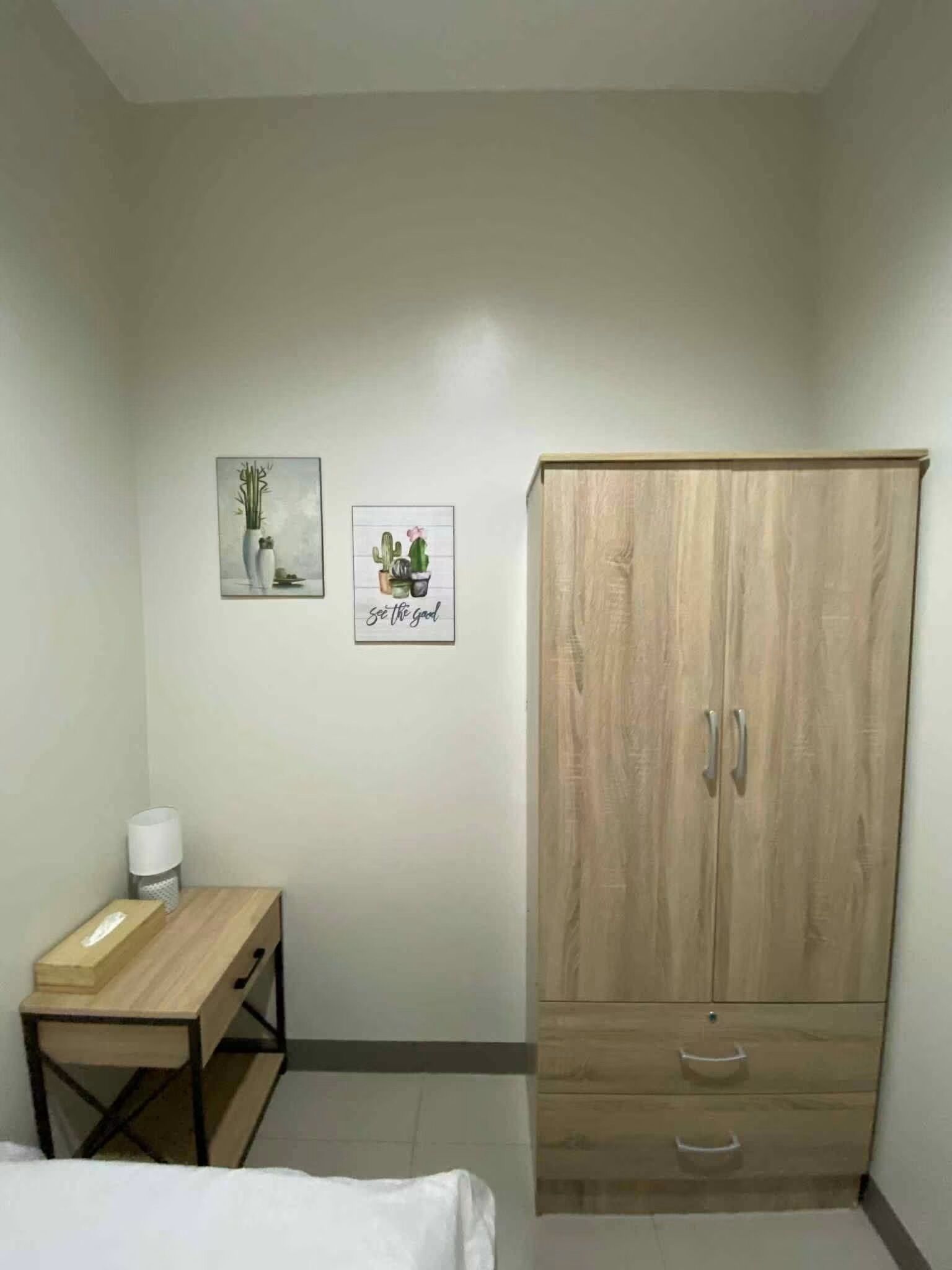 Une chambre à coucher avec une armoire en bois, un petit bureau et deux tableaux accrochés au mur.