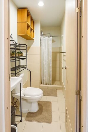 A bathroom with a toilet, sink, shower, and a shelf with toiletries. - Cosy Family staycation Casa De Nordeka Felix (Cainta)