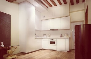 A compact kitchen with white cabinetry, a built-in oven, and a coffee maker on the countertop.