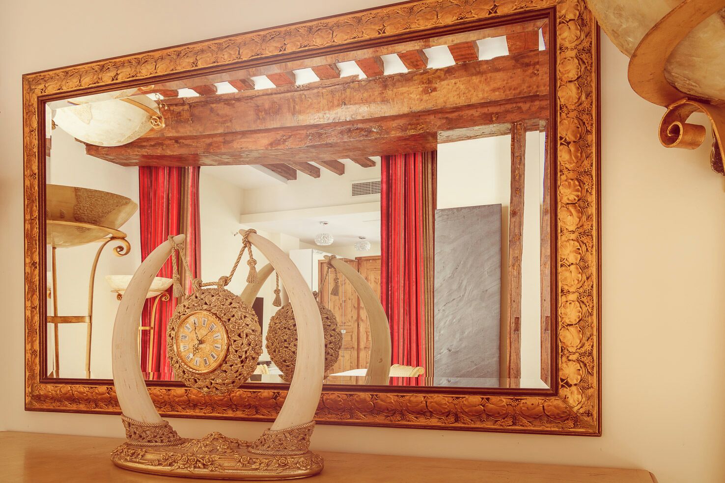A large ornate mirror with a wooden frame and a decorative clock in front of it.