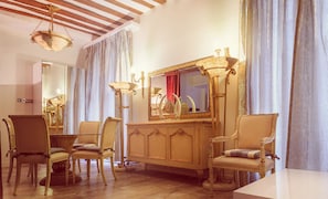 A room with a wooden cabinet, two chairs, a table, and a mirror with a decorative frame.
