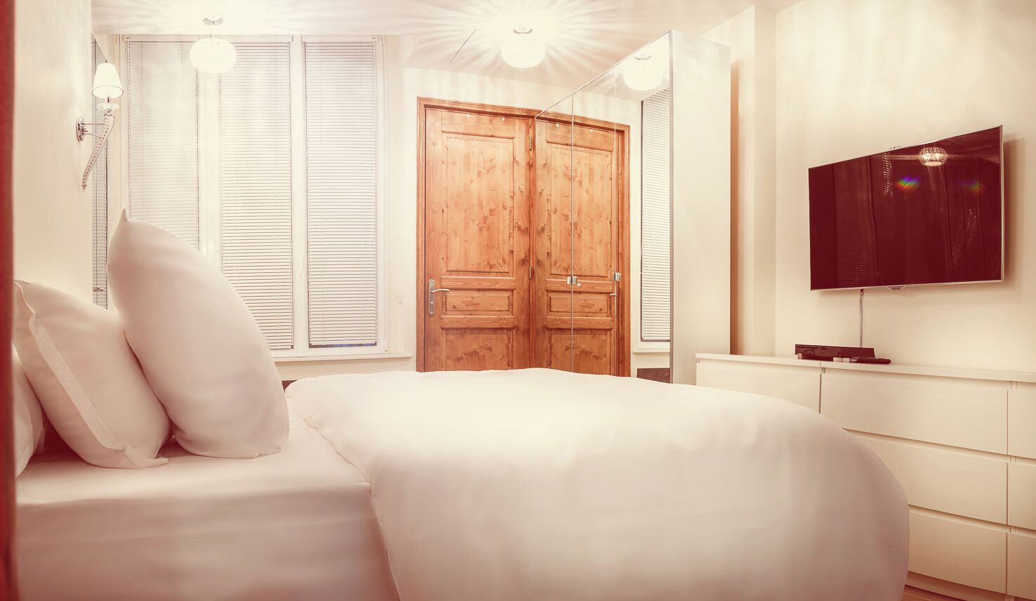 Een slaapkamer met een bed, een houten garderobe, een televisie en een raam met jaloezieën.